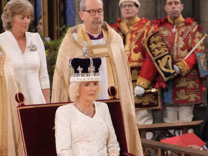 Queen Camilla wore a white silk dress with symbolic floral embroidery by Bruce Oldfield.