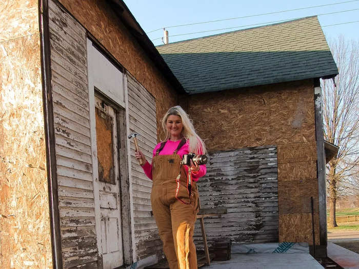 Katie standing on the porch with a drill in a neon pink shirt