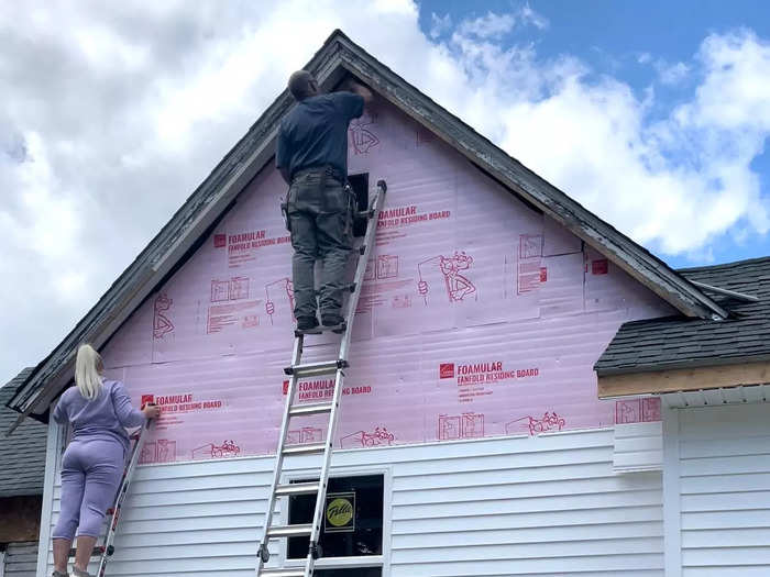 Katie and her father installing siding at the very top of the house.