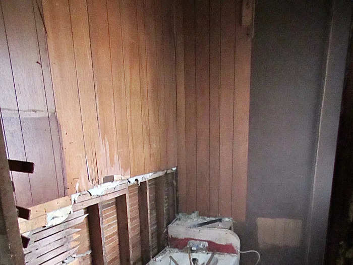 A destroyed bathroom with wood paneling falling off the walls