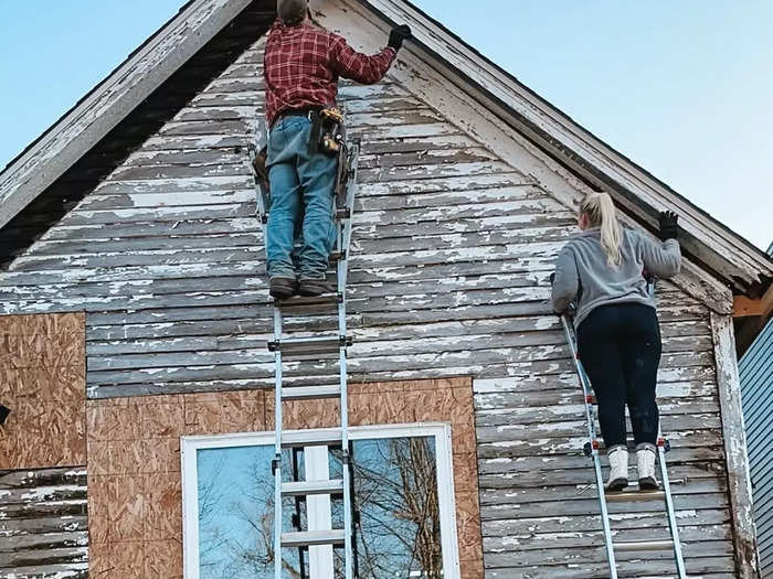 Katie and her father on side-by-side ladders fixing the roof