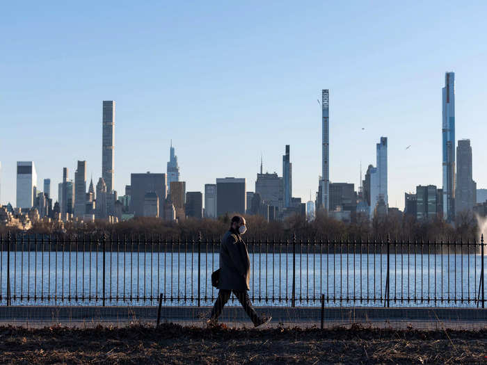 A person wearing a mask walks along the Jacqueline Kennedy Onassis Reservoir in Central Park with a view of Billionaire