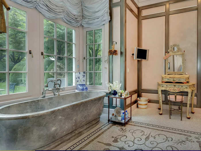 One of the bathrooms attached to the primary suite features a marble bathtub and a TV for prime relaxation.