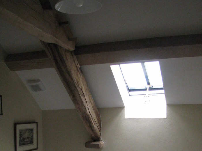 A modest bathroom also features exposed beams, as well as cream tiles and a white bathtub.