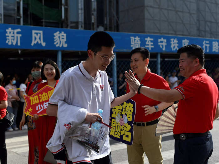 People sometimes volunteer to cheer on students with signs and high-fives, like these adults in Beijing.