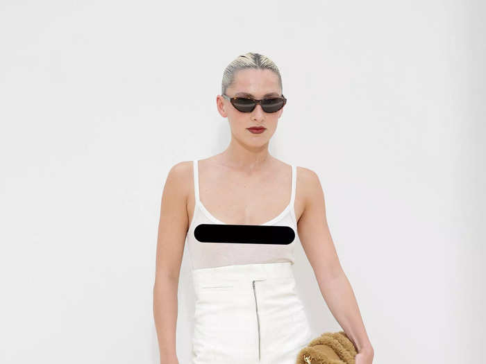 Elena Mottola arrived at the fashion show in a sheer, white top and high-waisted shorts that covered her torso. Thigh-high brown boots and sunglasses completed the look.