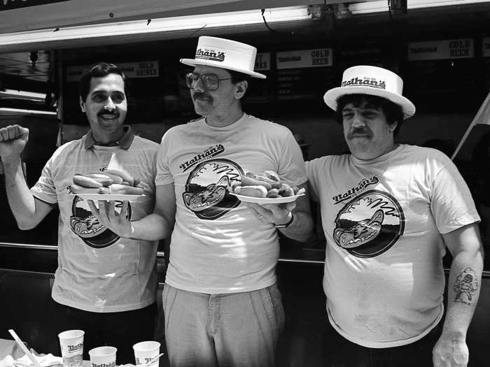 Here, three unidentified contestants pose with plates of hot dogs prior to the 1987 Nathan