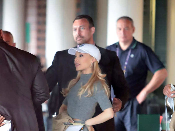 Ariana Grande went for a polished, sporty look in a gray, high-neck top with a matching, ankle-length skirt to attend a Wimbledon game. She added black, pointed-toe heels — and, in a departure from her typical hairstyle, she wore her hair down with a baseball cap.