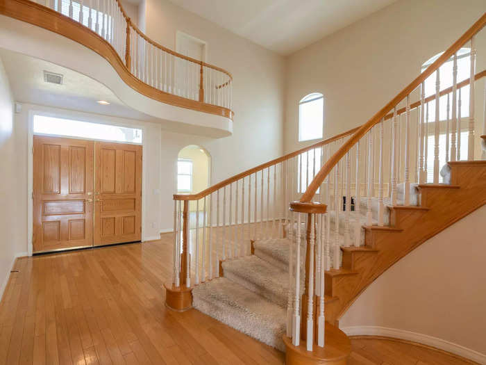 The entryway had tall ceilings, barren white walls, and wood finishing on the double doors and staircase.