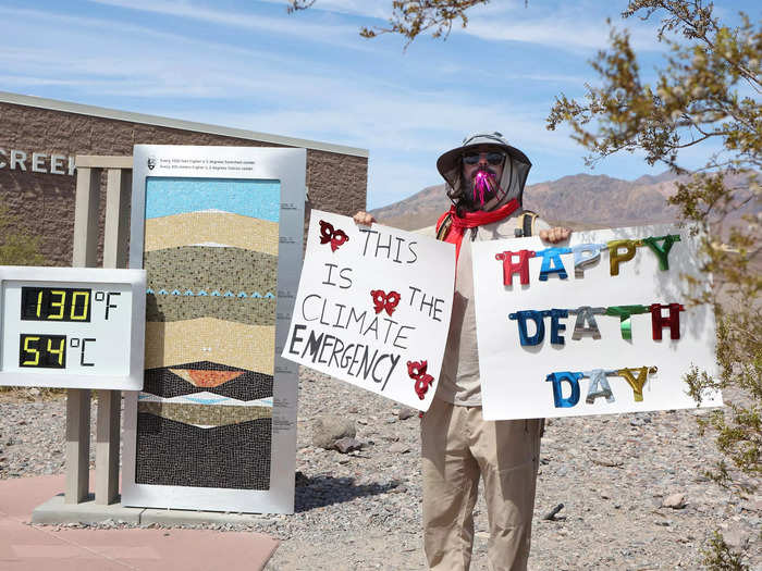 Among the recent visitors was this man wearing a sunhat and sunglasses, standing in front of the digital temperature display at Furnace Creek holding a "Happy Death Day" poster and another that read: "This is the climate emergency."