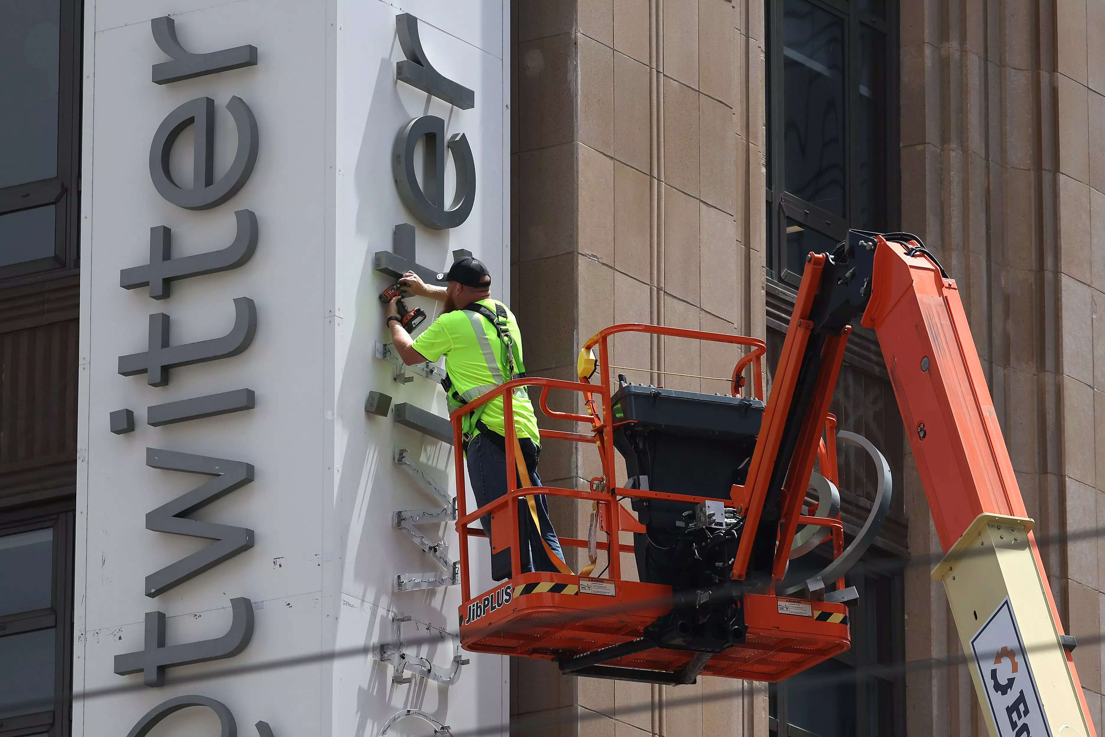 A worker in a high-visibility jacket using a cherry picker to remove letters from a large sign that reads "Twitter"