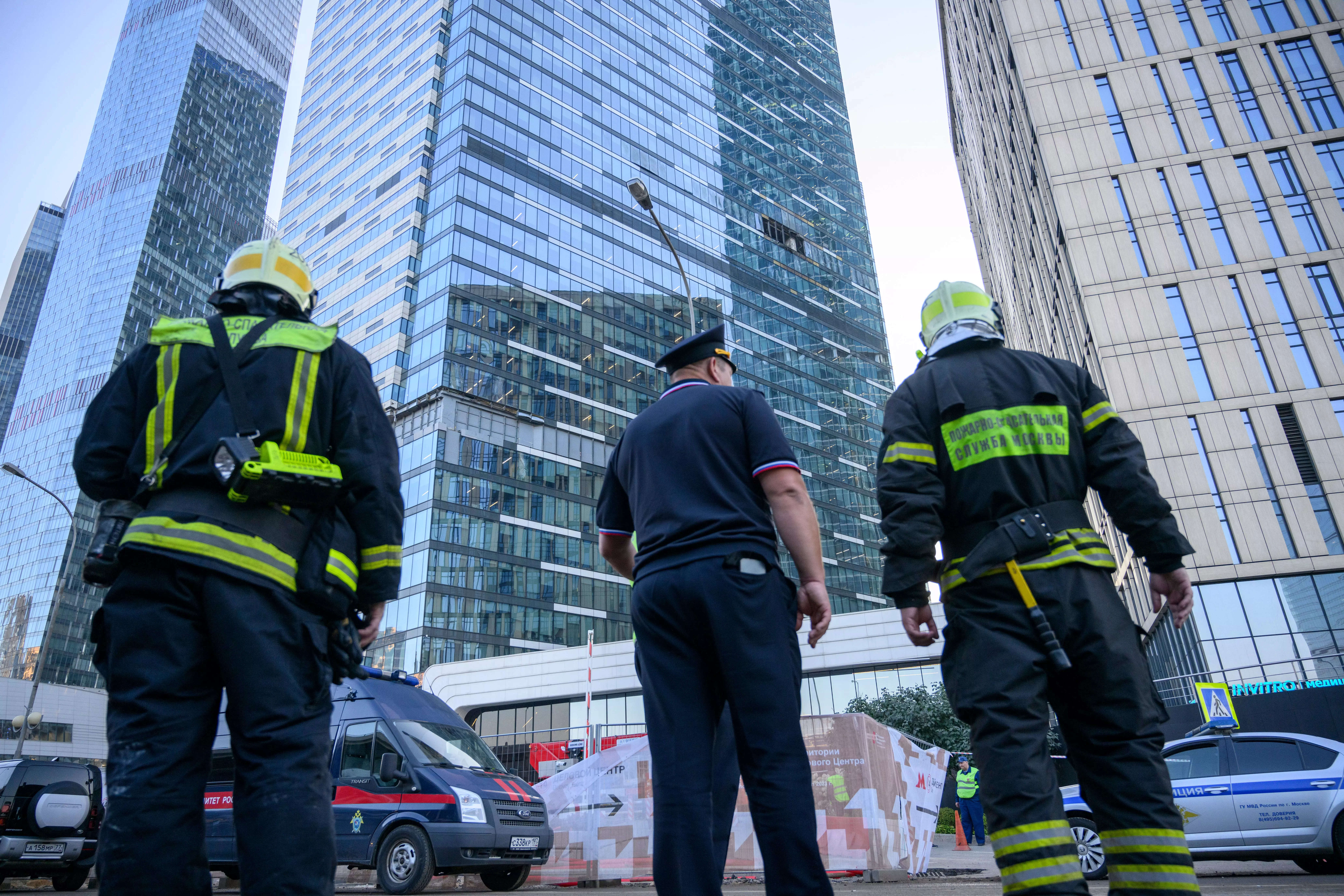 Firefighters and a police officer stand next to a damaged building in the "Moscow City" business district after a reported drone attack in Moscow, Russia, early Tuesday, Aug. 1, 2023.