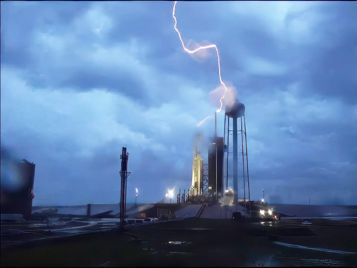 A picture shows Falcon Heavy on its launchpad. A bolt of lightning hits both its dfelctor tower and the rocket.