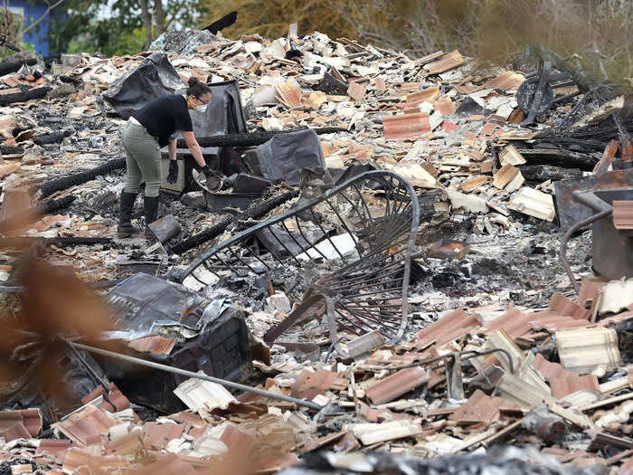 In Kula, a district about an hour inland, a woman wore a face mask and boots to look through the remains of a downed home.