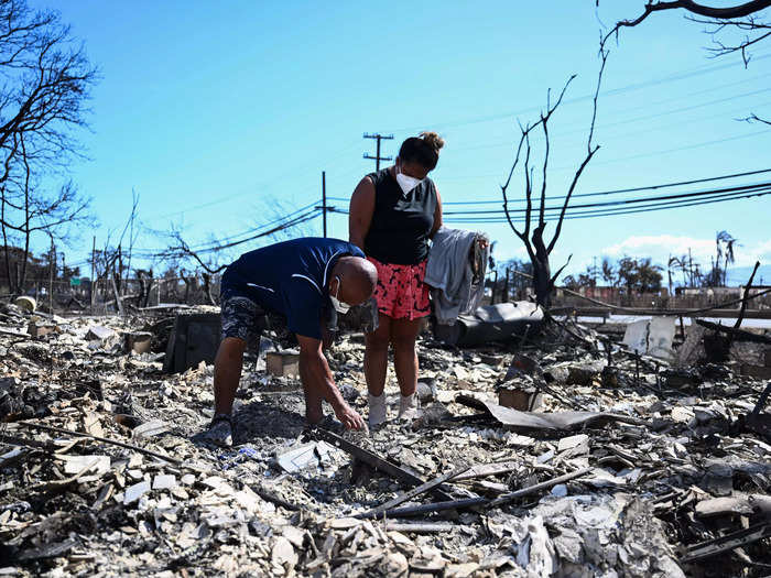 Two Lahaina residents were photographed wearing masks and sifting through the ashes of their homes.