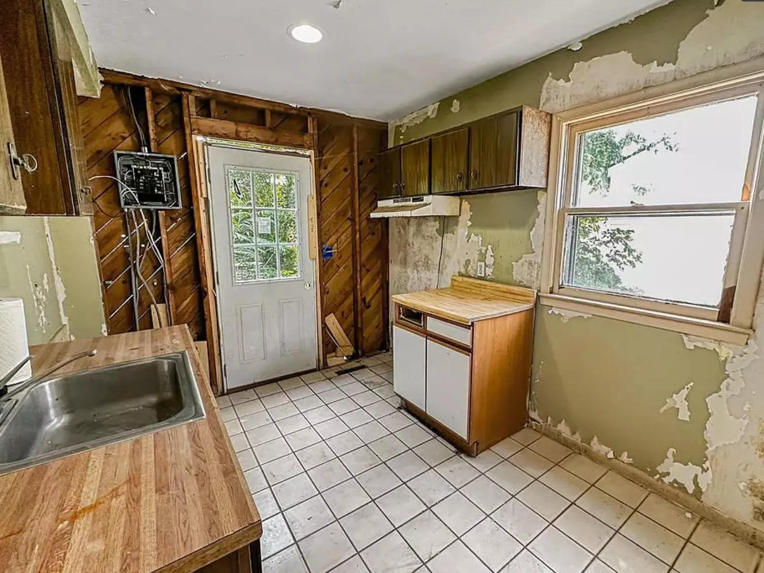 The kitchen of the $1 house in Michigan. The paint is peeling from the walls and the floor is covered in a layer of grime.