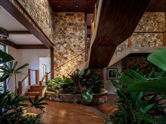 The entry lobby is lush and welcoming, with plenty of plants, stone walls, and a floating staircase.