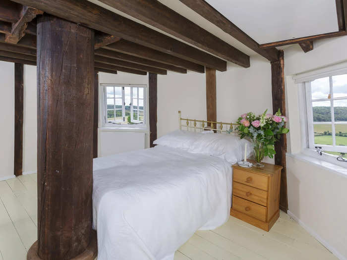 The bedroom has a vaulted ceiling, wooden beams, and windows that look out to the countryside.