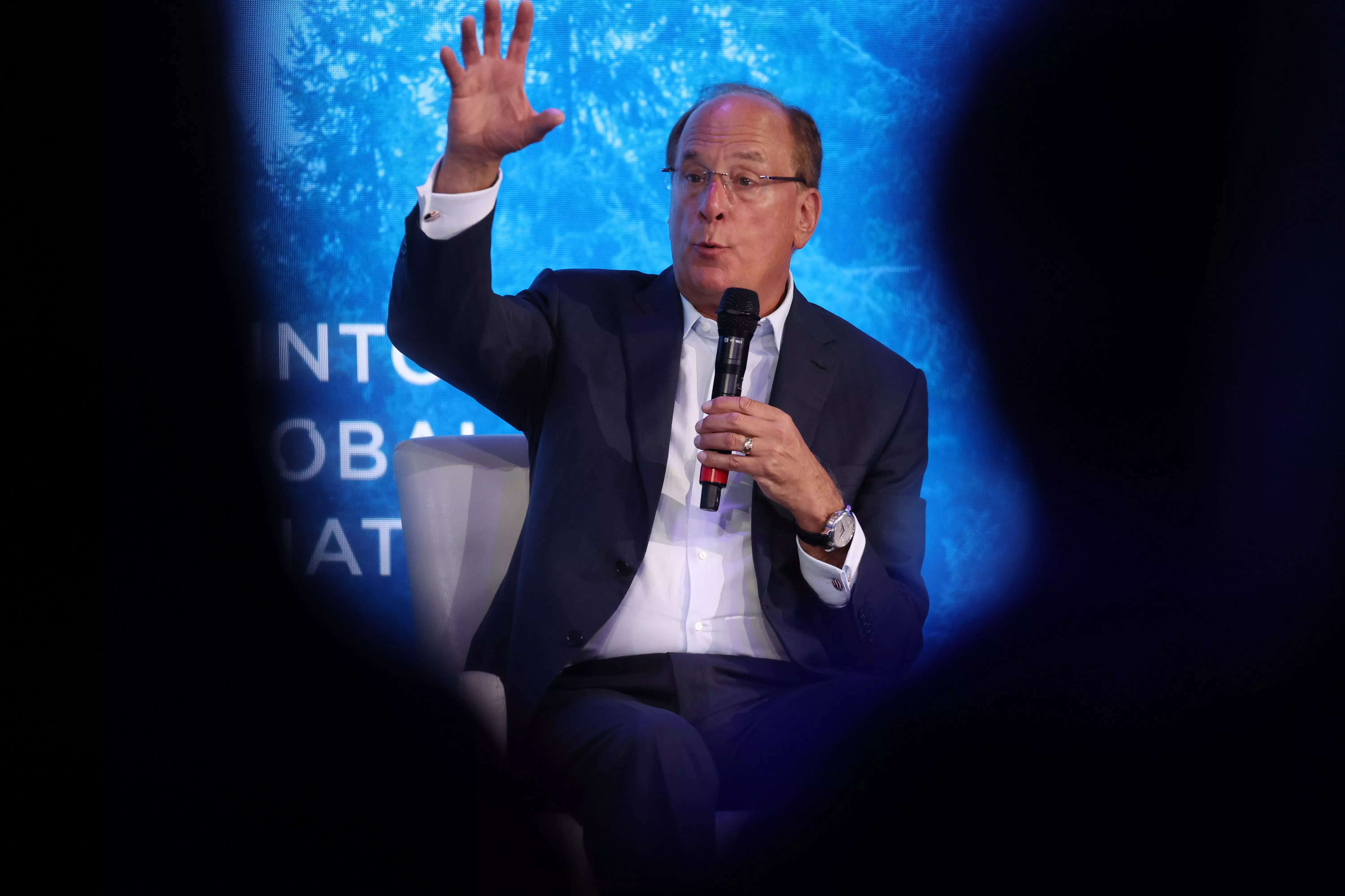 BlackRock CEO Larry Fink raises his arm in front of a blue background.
