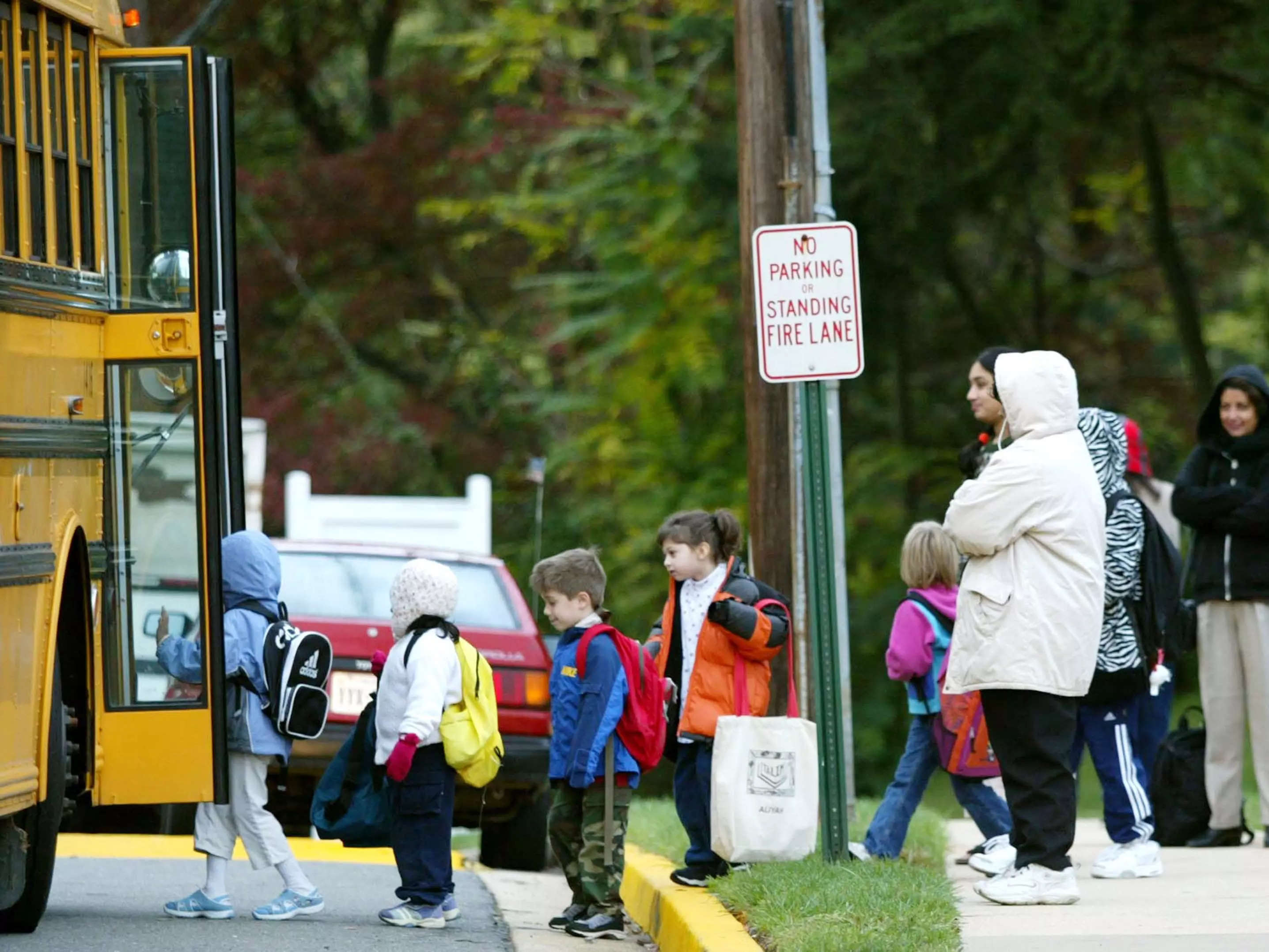 A group of parents huddle around a designated stop as their kids board a school bus.