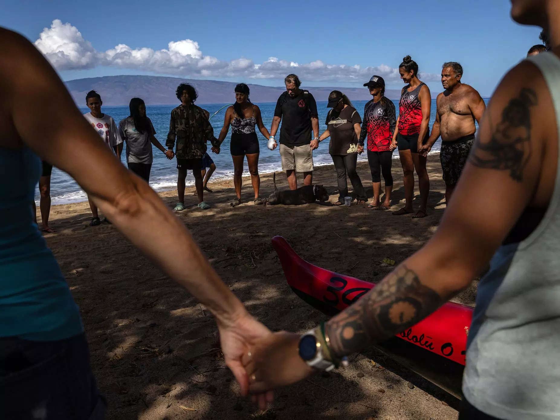 Members of the Lahaina Canoe Club hold hands in prayer in honor of a member who died in the fires. The outing was the first time the club members, many of whom lost their homes, had paddled together since the fires.