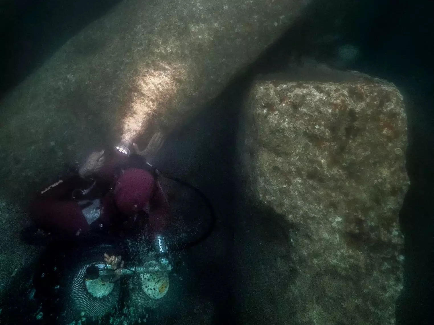 A diver looks at a huge rock column underwater.