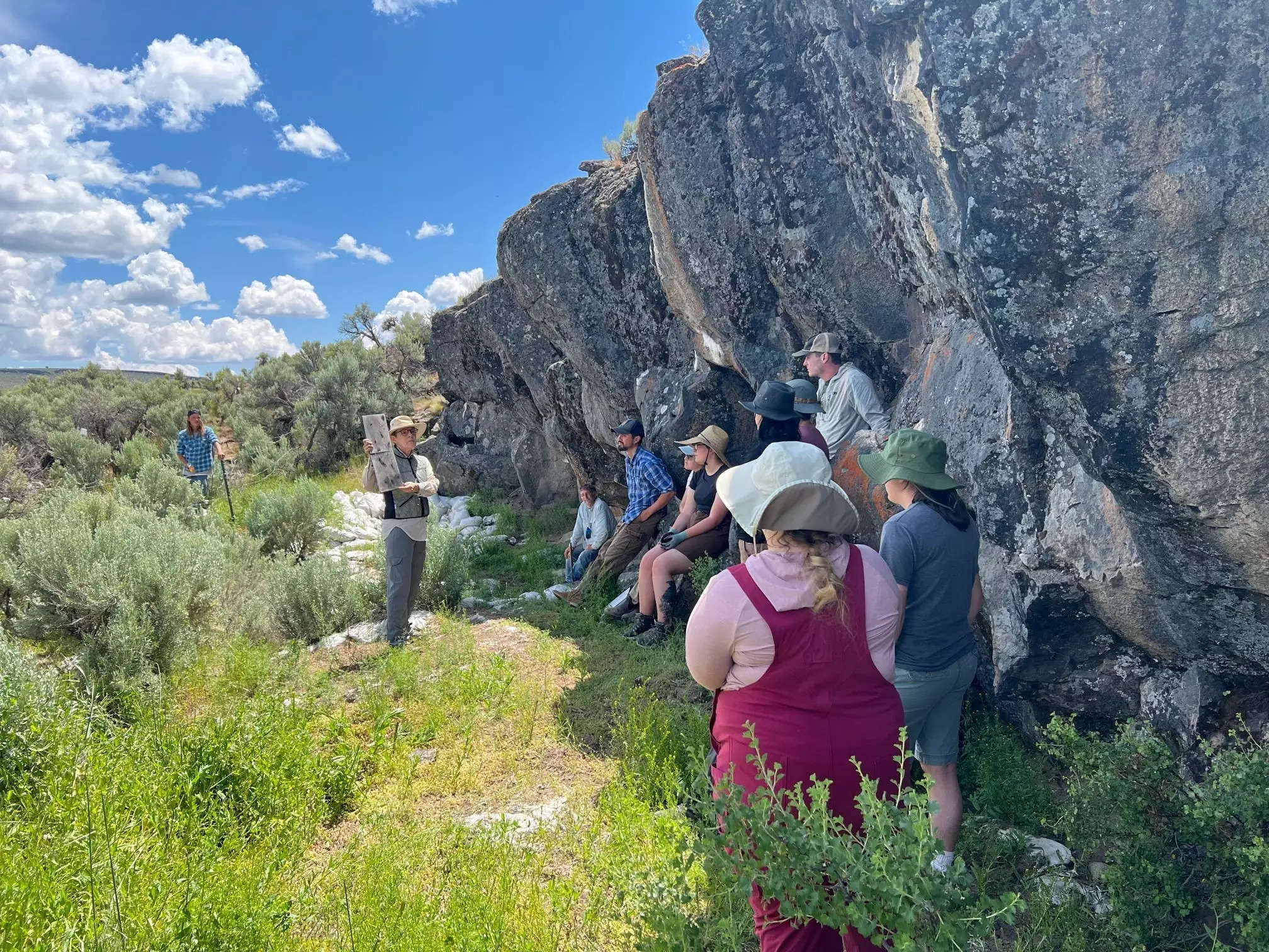 Several people stand near the Rimrock Draw Rockshelter, an archeological site containg stone tools that are over 18,000 years old