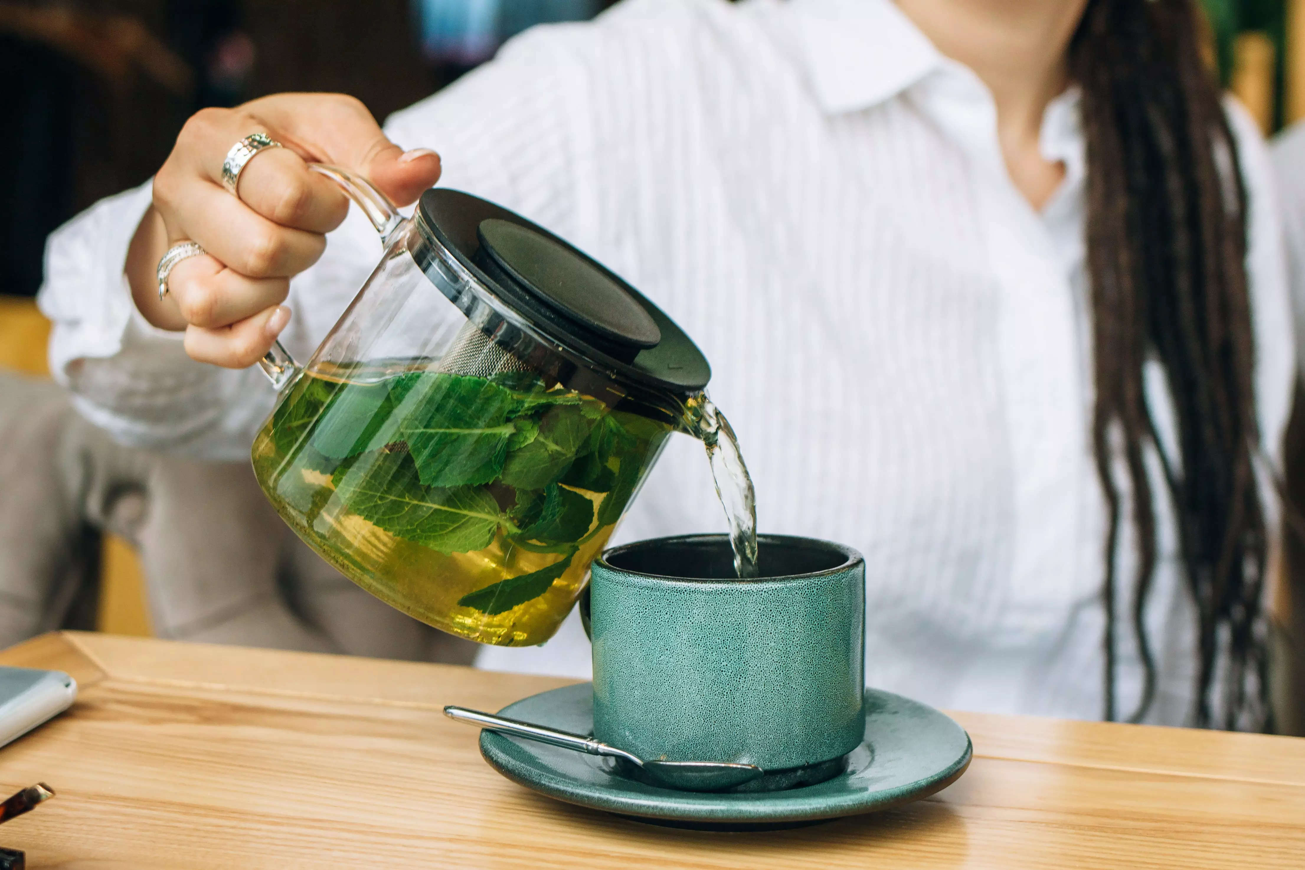 Green tea being poured into a teal mug.