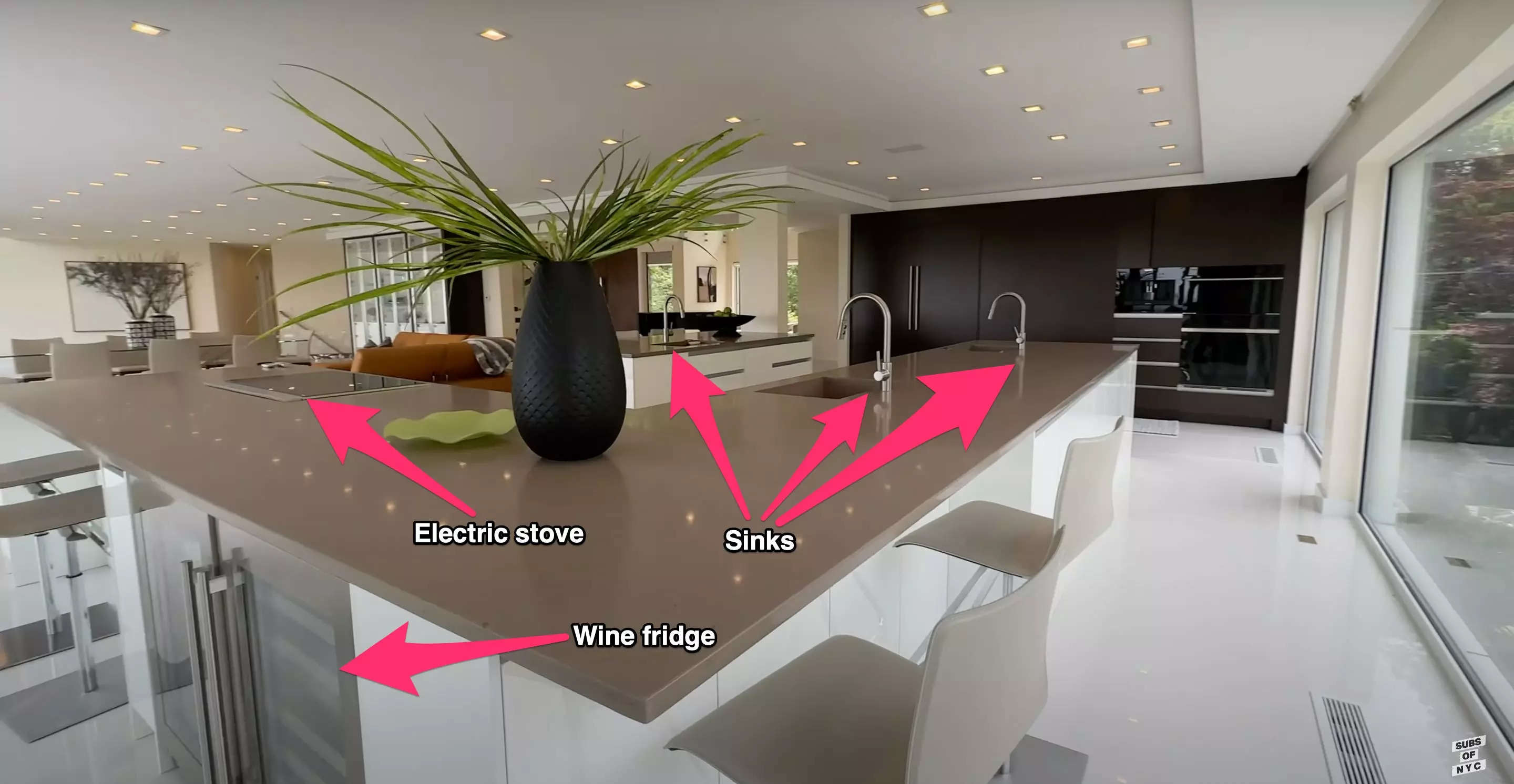 A modern kitchen with pink arrows pointing to the wine fridge, electric stove, and three sinks.