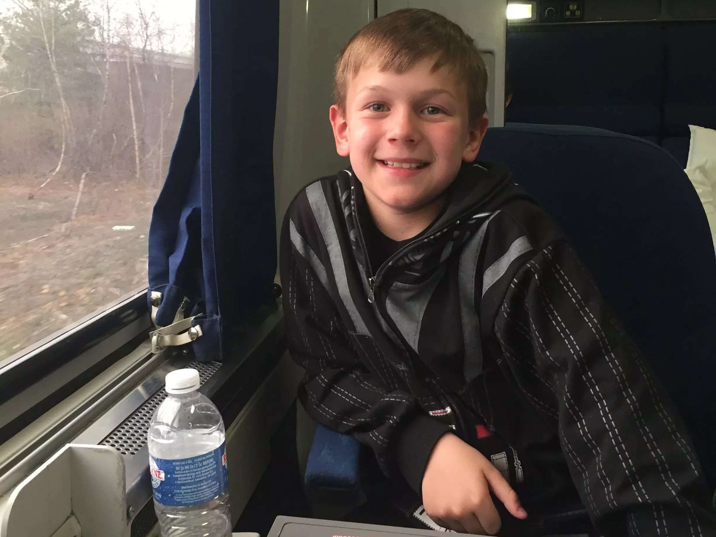 A boy seated on a train next to a window, smiling.