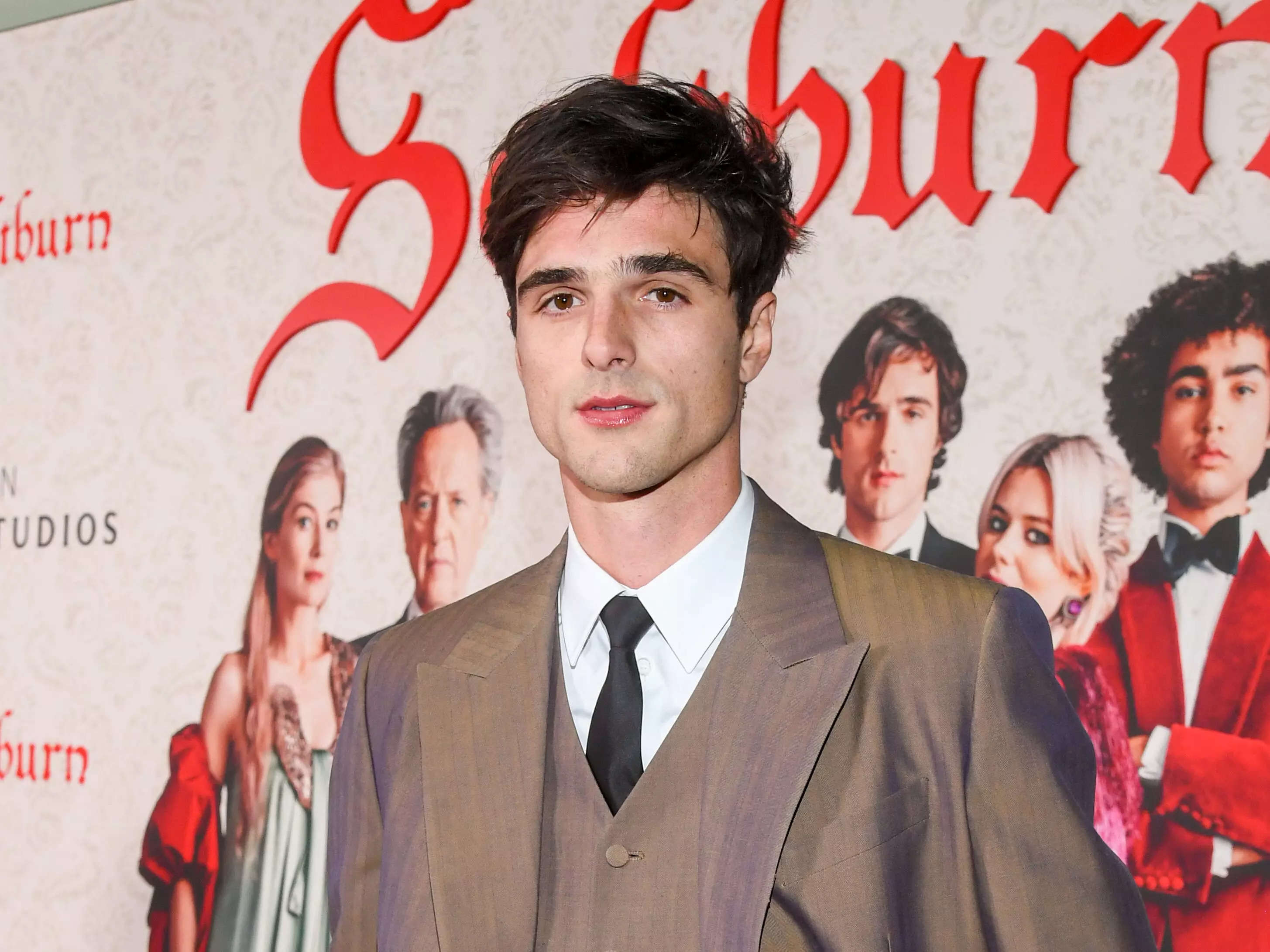 jacob elordi in a brown suit standing on the saltburn red carpet with his hands in his pockets