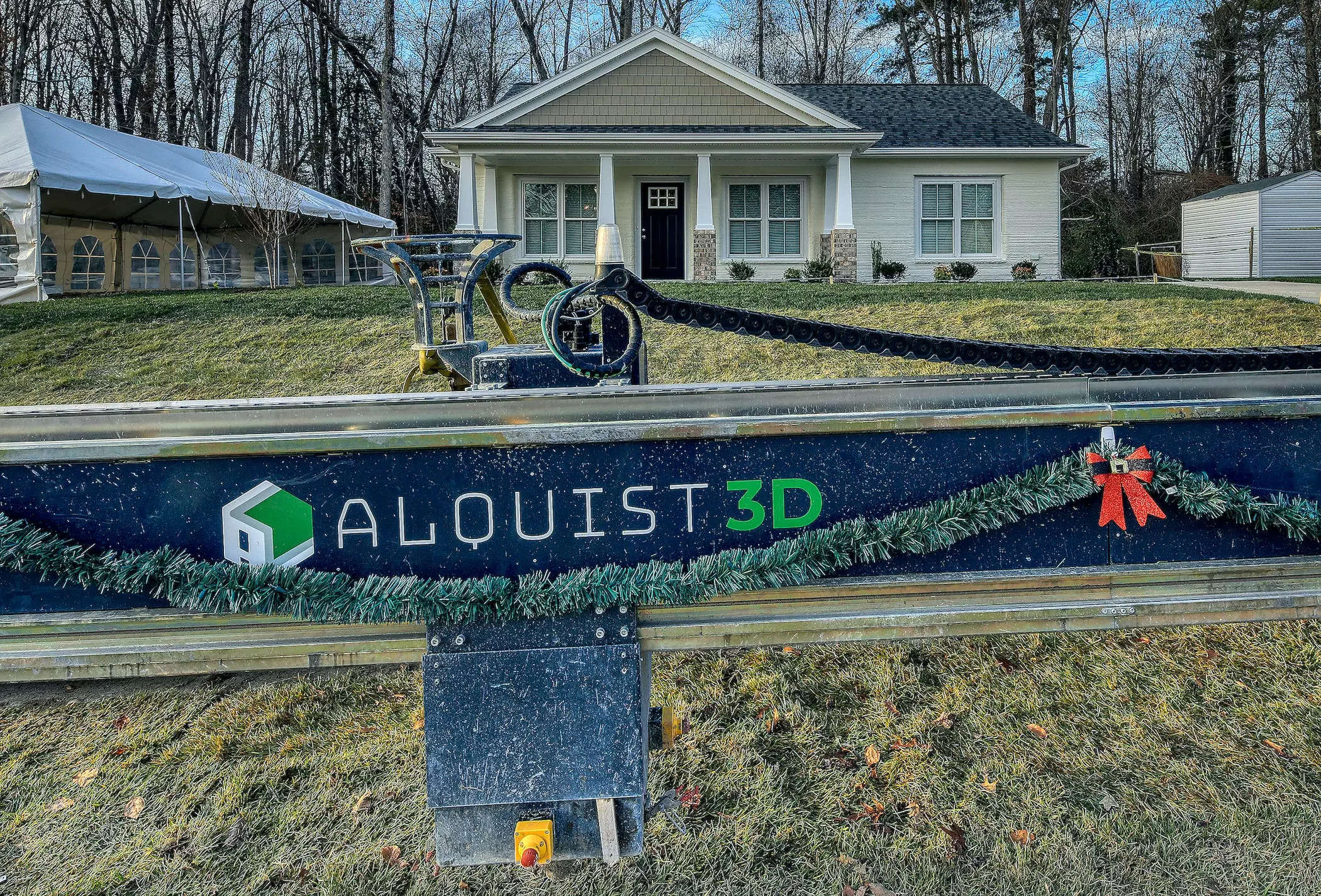The exterior of the Habitat for Humanity 3D printed house in Virginia behind a patch of green grass, an Alquist 3D barricade, walkway