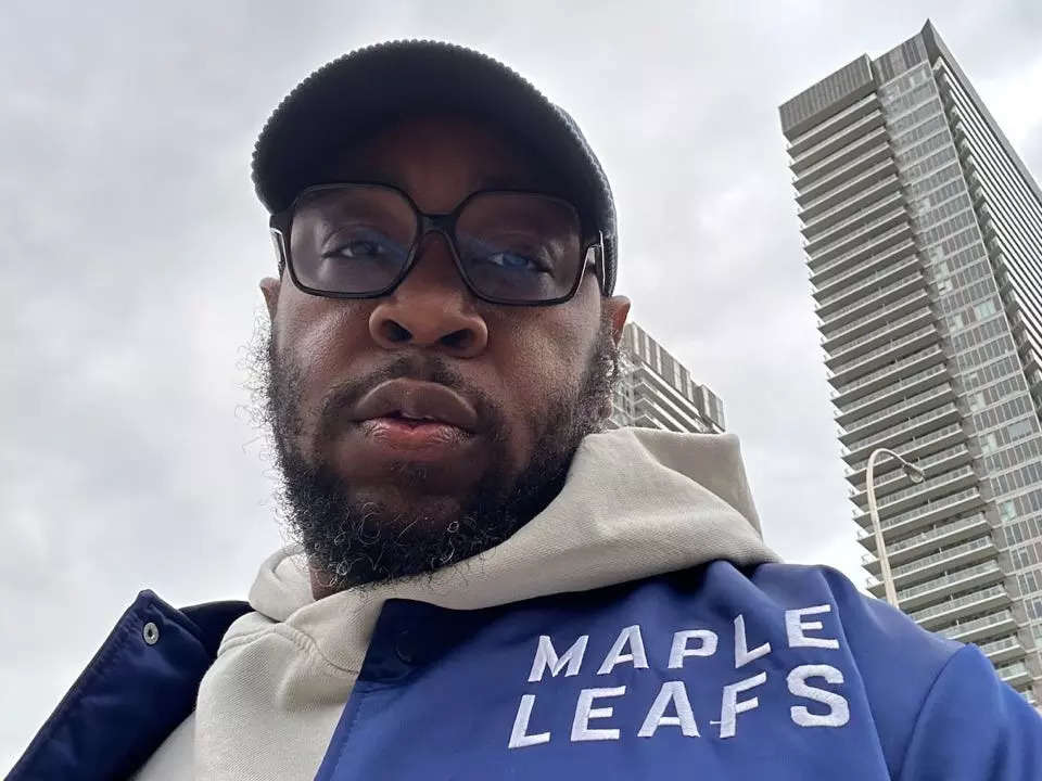Stephen Clarke poses under a gray sky wearing a blue Toronto Maple Leafs jacket