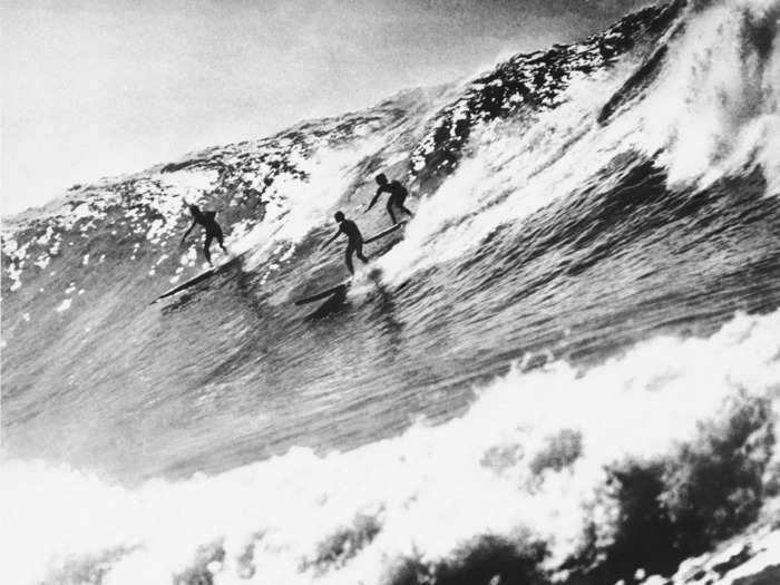 1953: Hawaiian surfers Buzzy Trent, Woody Brown, and George Downing surf a 19-foot wave at Makaha, near Waianae, Oahu.