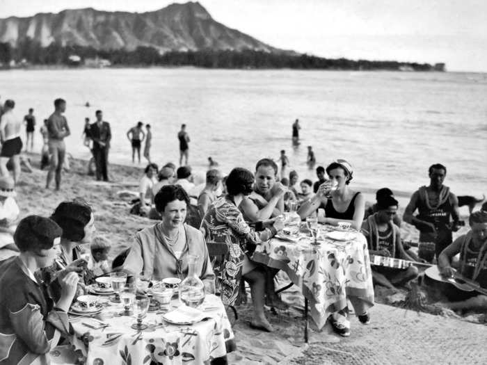 1936: People enjoying their lunch at tables on the beach in front of the Royal Hawaiian Hotel on Waikiki Beach, Honolulu.