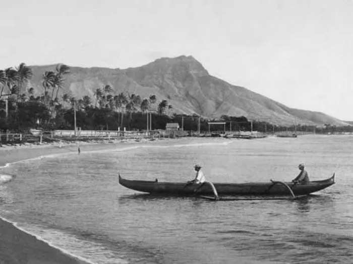 Early 1900s: Two local men in their raft rest by the beach at Waikiki Bay.