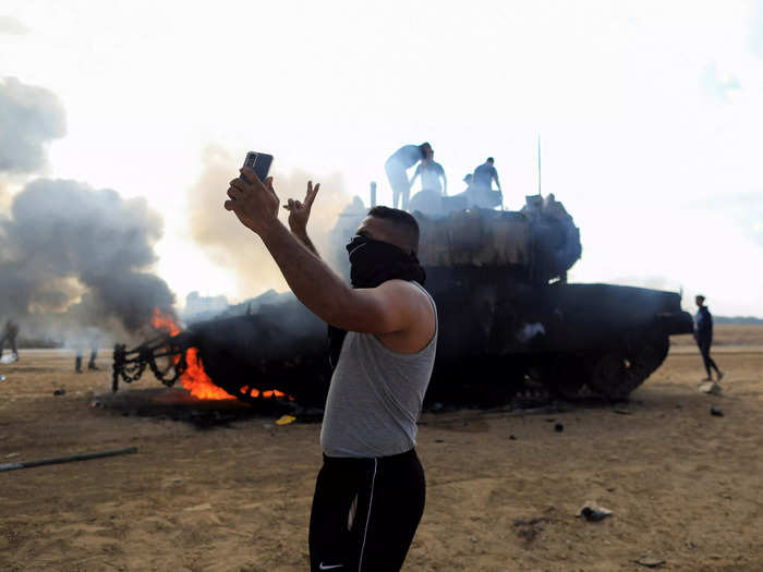 9. A Palestinian man takes a selfie in front of a burning Israeli tanks