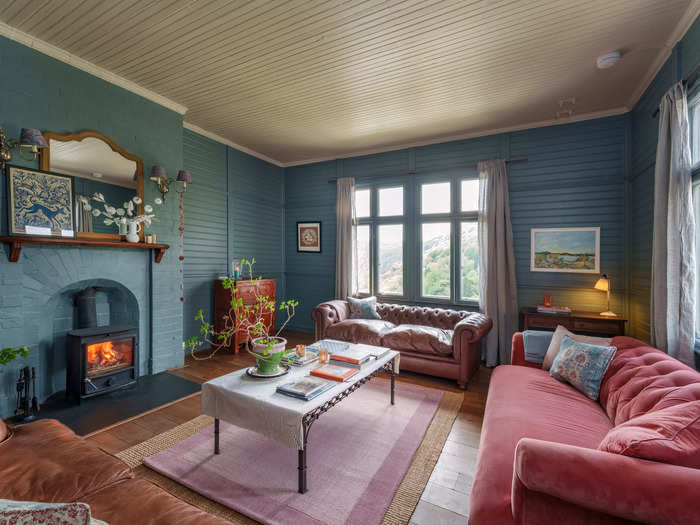 One of three living areas on the ground floor, featuring a fireplace and windows overlooking the surrounding woods.