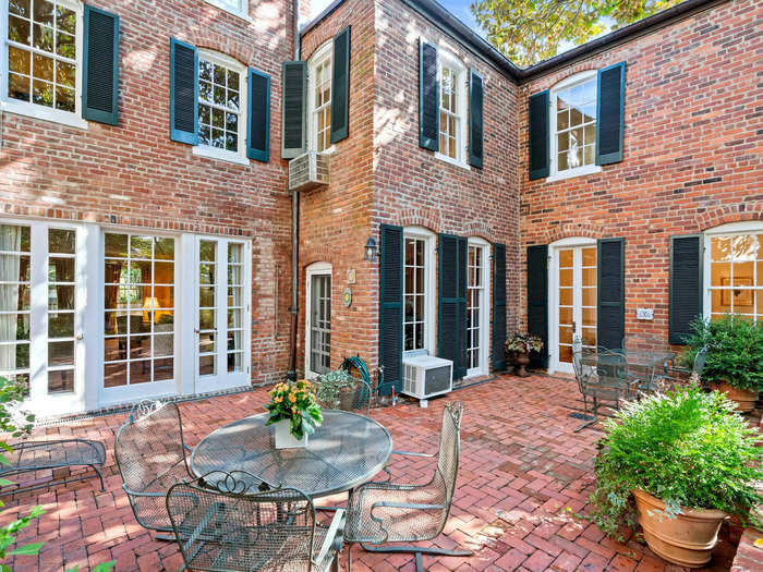 The backyard features a dining patio, lush walkways, and an ornate stone fountain fixture.