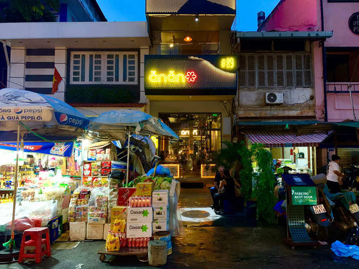 The entrance is hidden behind a market stall selling soft drinks and instant noodles.