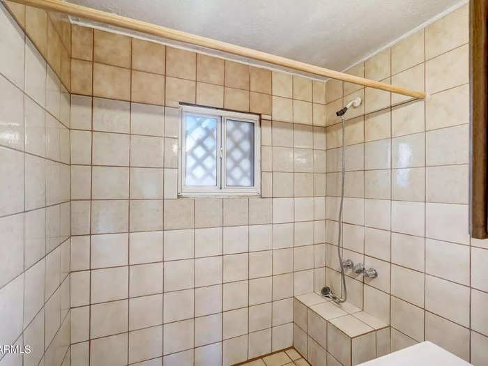 One of two bathrooms in the home has a window in the bathtub and has walls covered in tile squares.