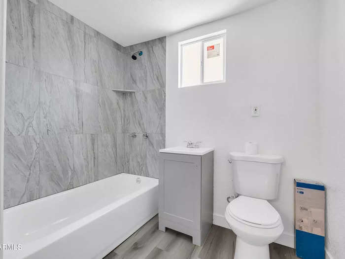 The bathroom has a marble-clad bathtub area and the same muted flooring as found in the rest of the home.