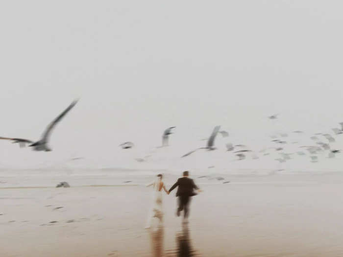 A couple is surrounded by birds on a beach in Tofino, Canada.