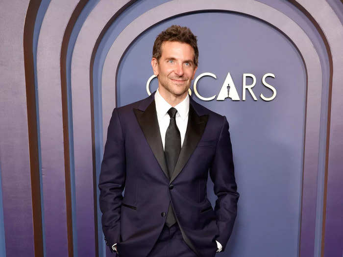 Bradley Cooper wore a navy suit with black lapels by Louis Vuitton over a white shirt and black tie.