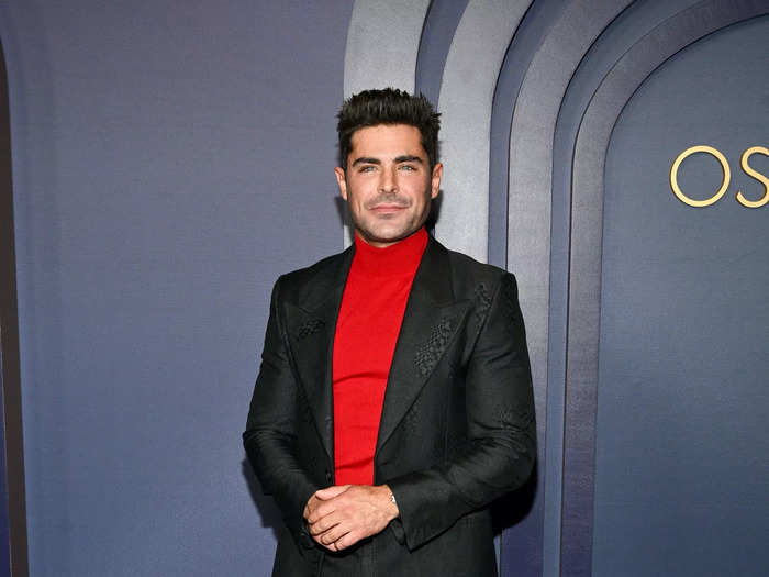 Zac Efron wore black pants and a matching blazer over a red turtleneck sweater. 