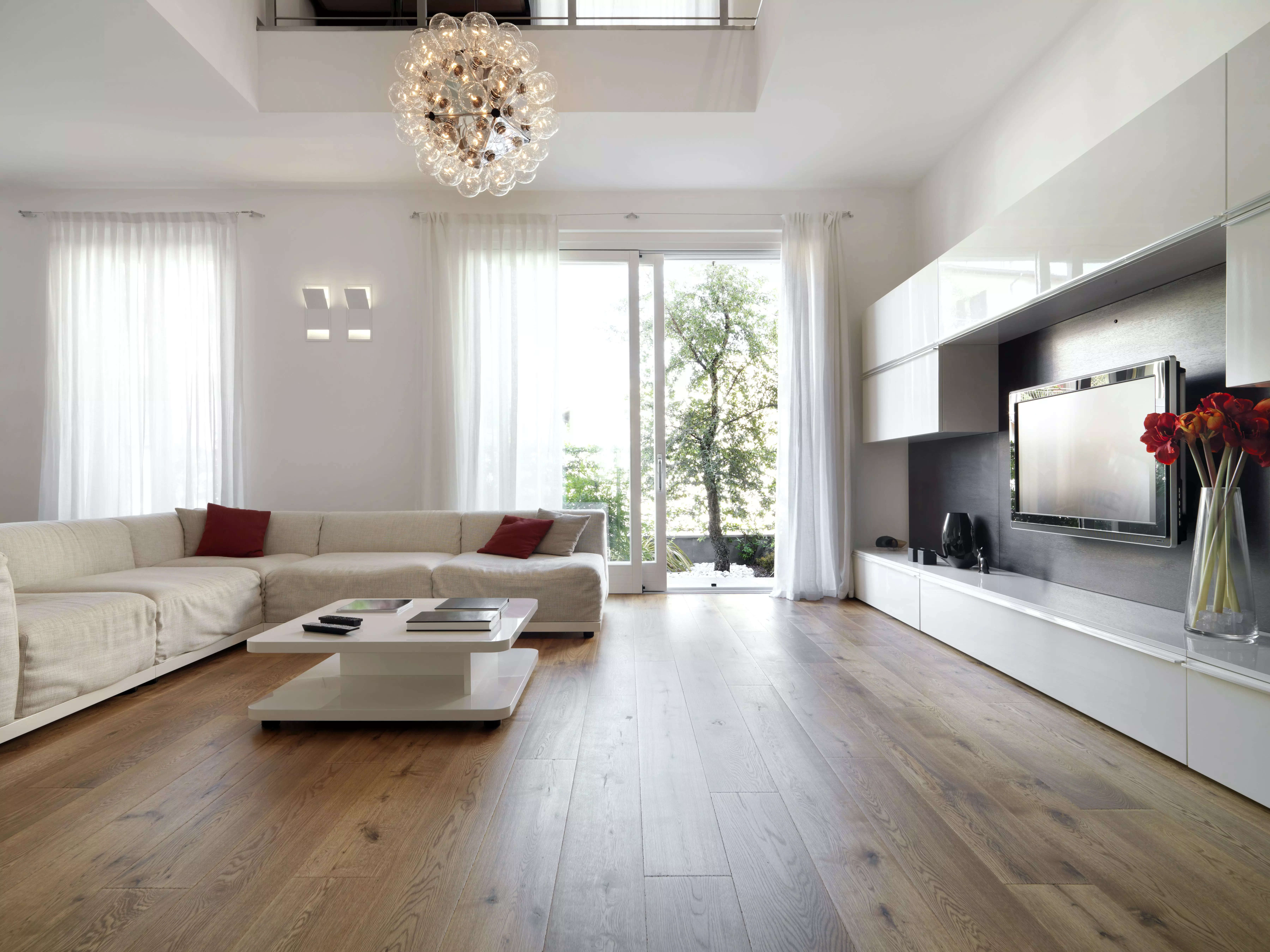 A living room with a white sofa, coffee table, TV, and bare hardwood floors