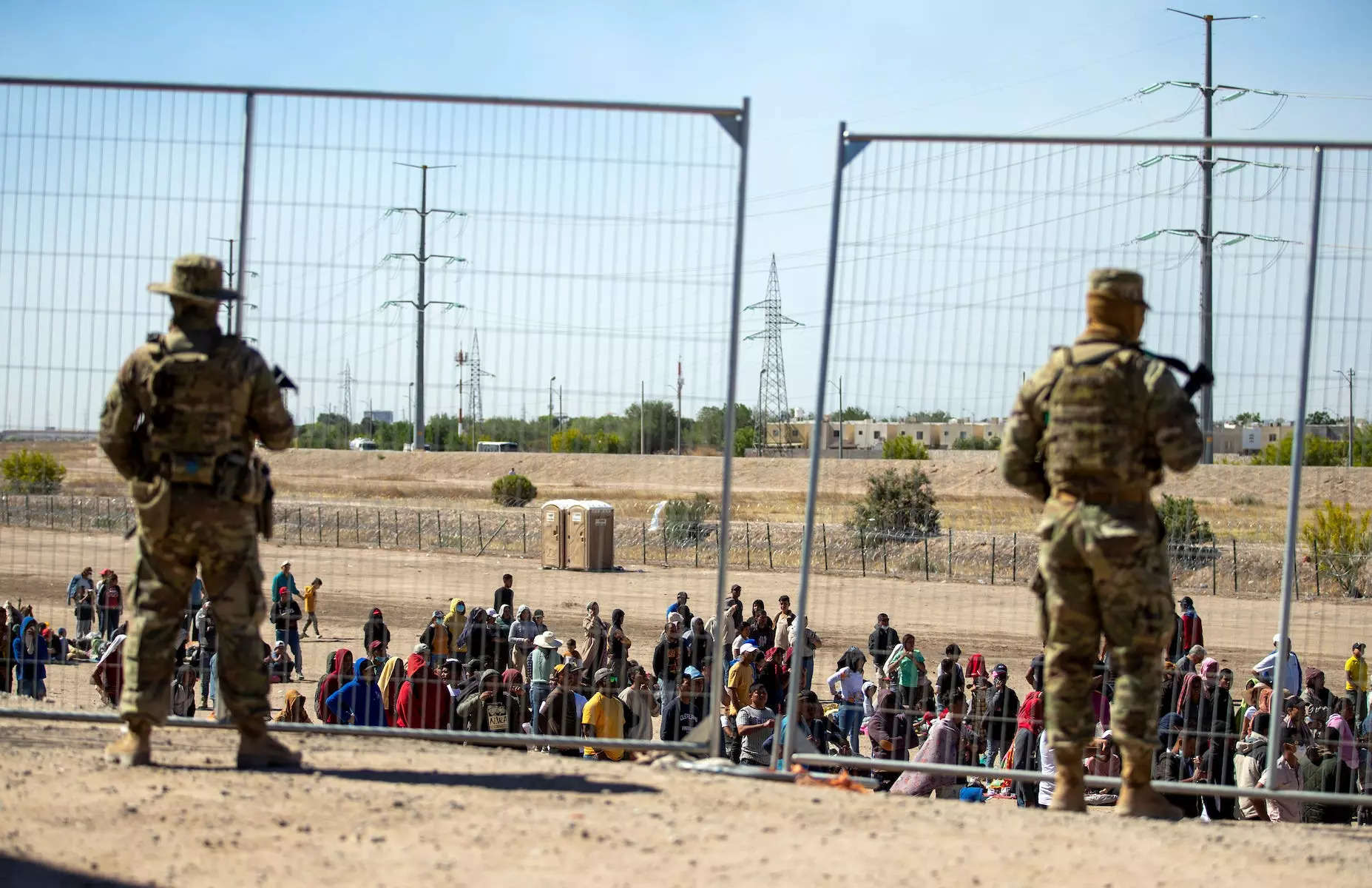 Migrants wait in line adjacent to the border fence under the watch of the Texas National Guard to enter into El Paso, Texas, May 10, 2023.