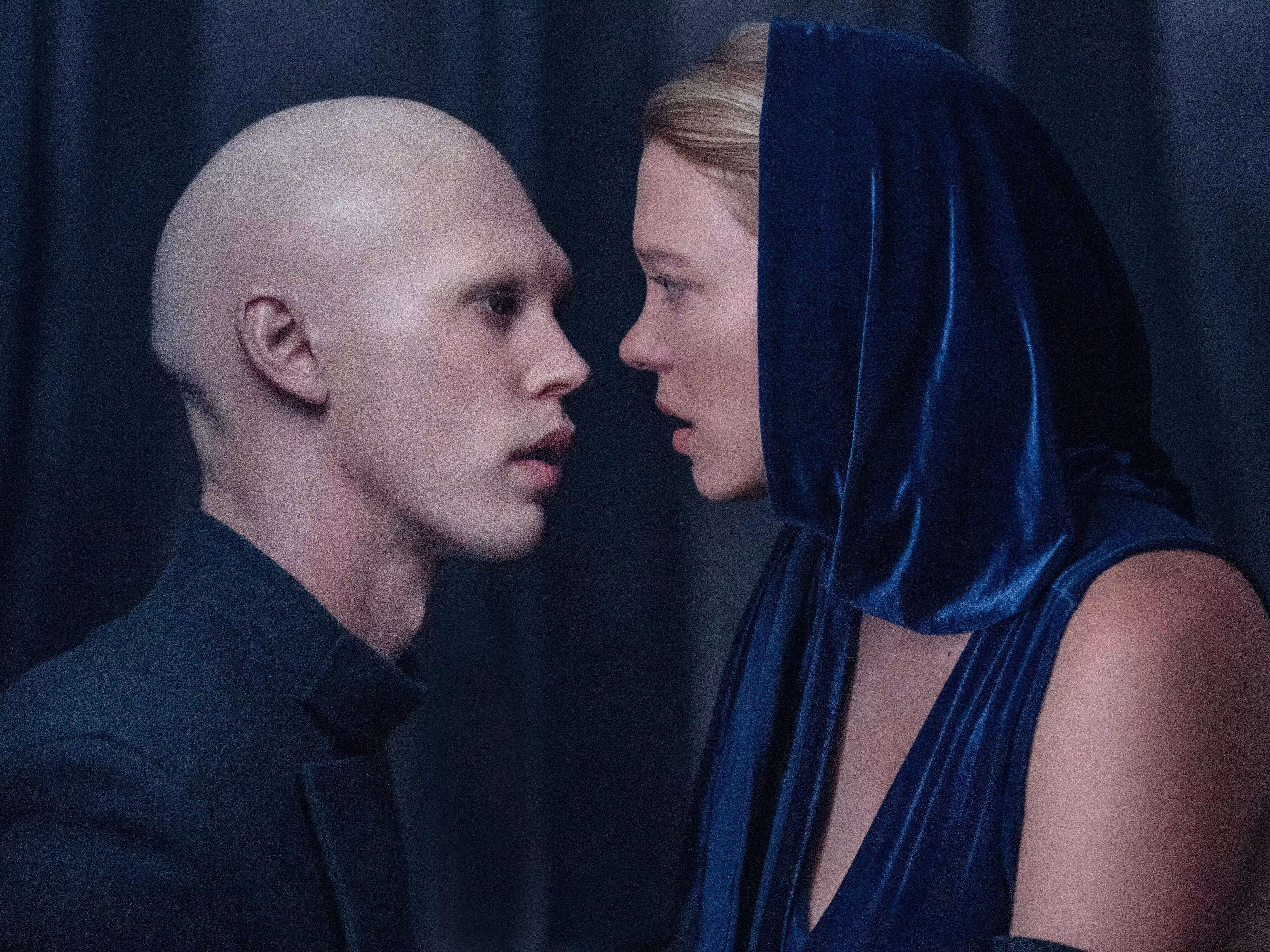 austin butler and lea seydoux in dune. butler as feyd-rautha is extremely bald, wearing a black high-collar jacket. seydoux as lady margot is wearing a blue velvet dress, with some fabric draped above her head