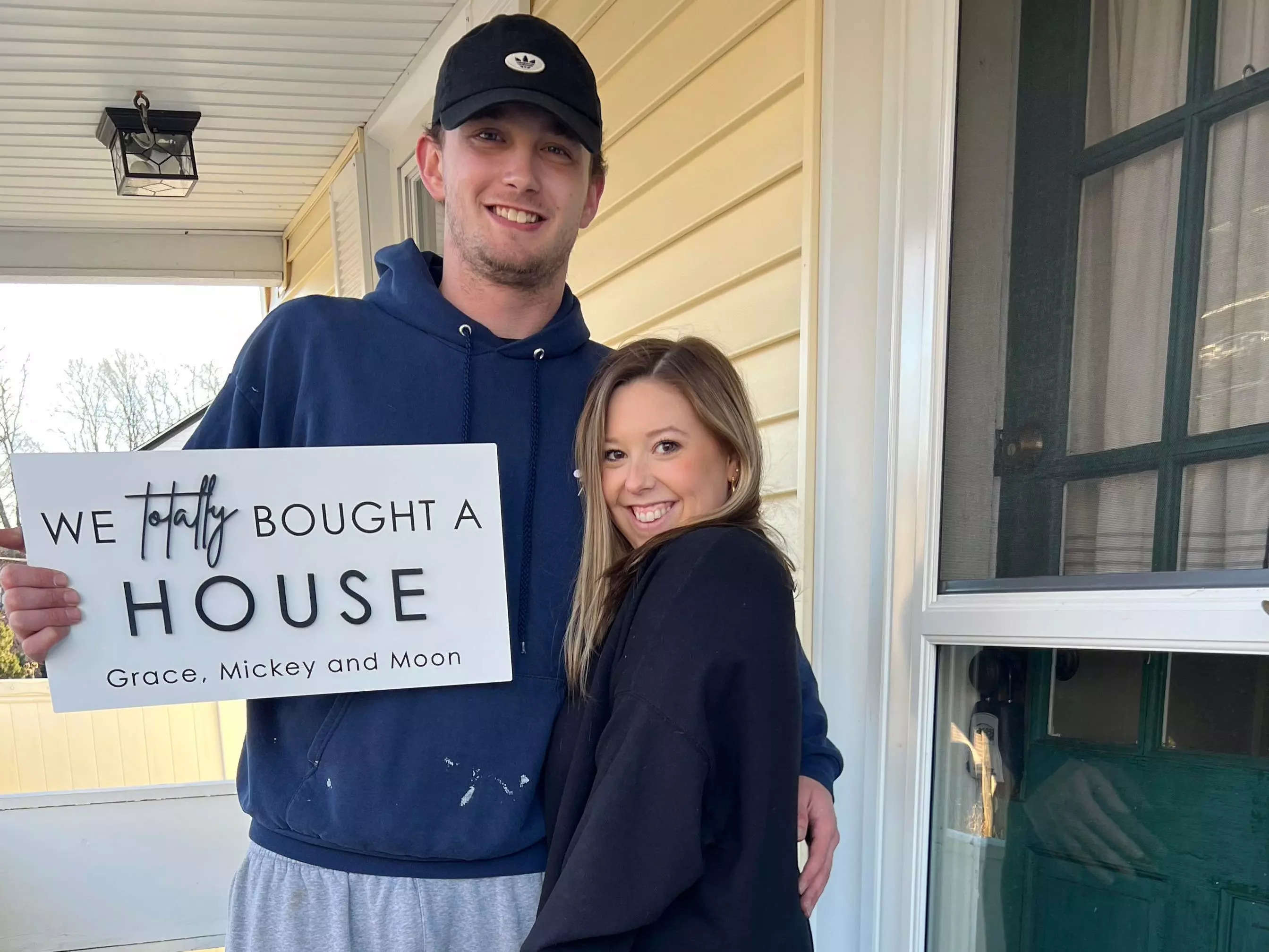Grace Lucchese and Mickey Ricard holding a sign that says, "We totally bought a house."