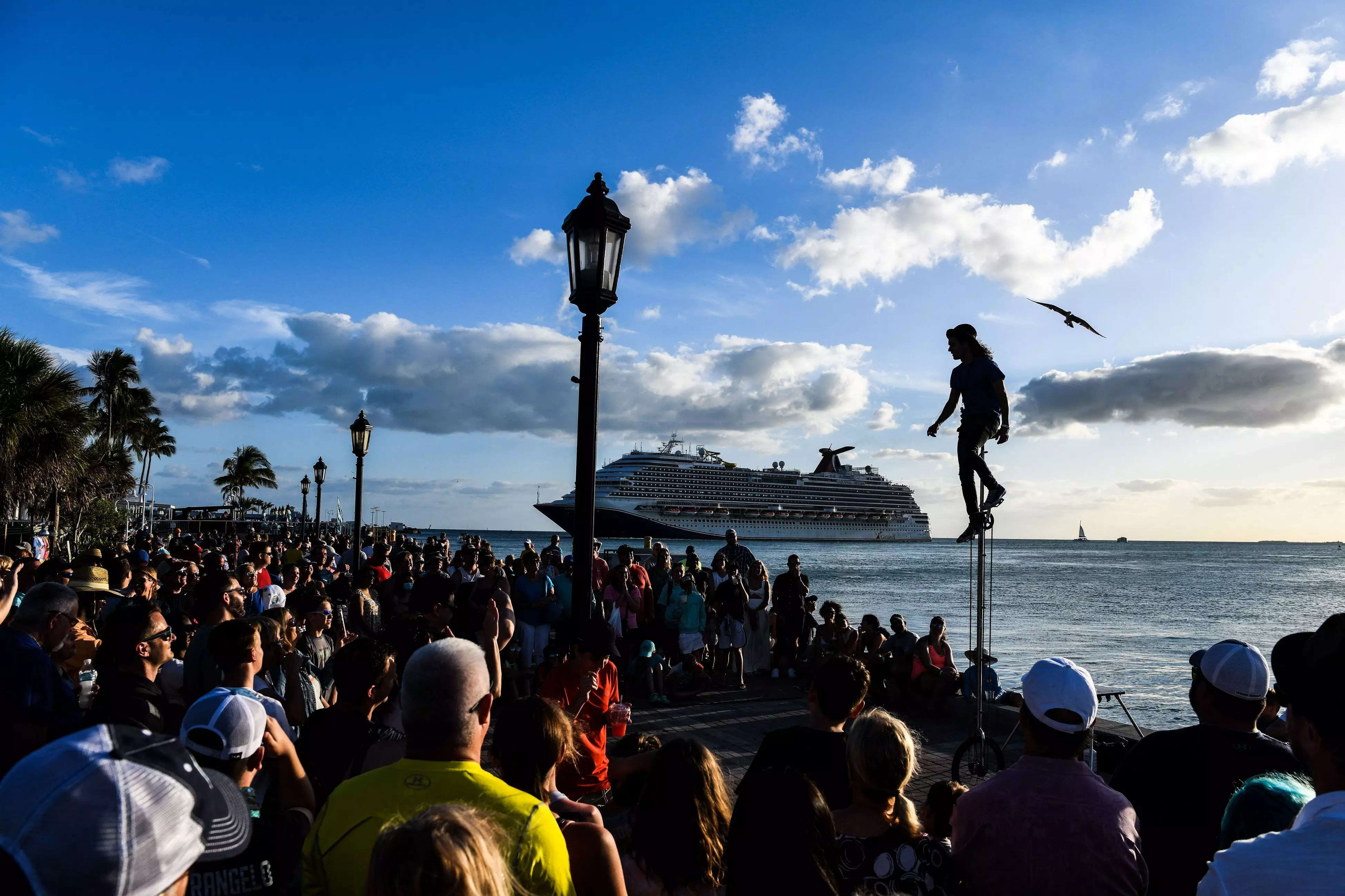 People watch an artist perform as the Carnival Dream cruise ship sails in Key West, Florida, on April 11, 2022